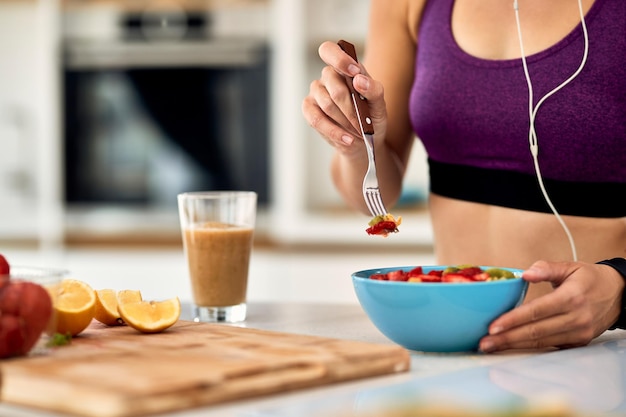 Closeup de atleta feminina com salada de frutas para um lanche na cozinha