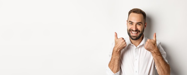 Foto grátis closeup de cara barbudo satisfeito na camisa branca mostrando os polegares em aprovação como e concordo positiv
