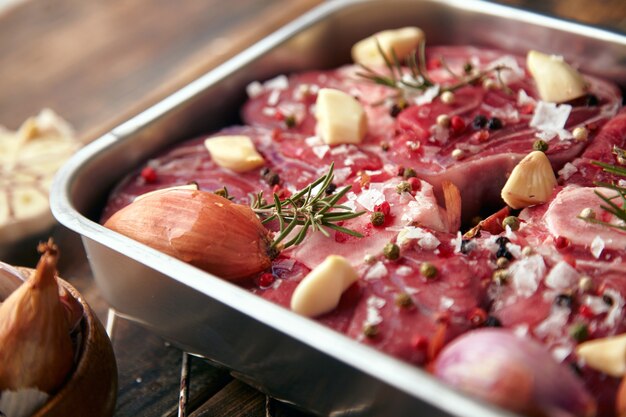 Closeup de carne em temperos de panela de aço ao redor: alho, alecrim, cebola