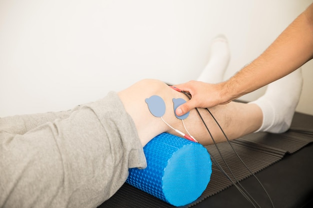 Closeup de eletrodos de posicionamento da mão do fisioterapeuta no joelho do paciente no hospital