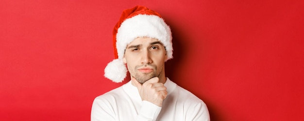 Closeup de homem bonito pensativo com chapéu de papai noel franzindo a testa e olhando para a câmera pensando em algo...