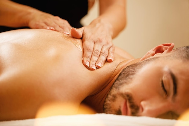 Closeup de homem desfrutando em relaxante massagem nas costas com mel no spa