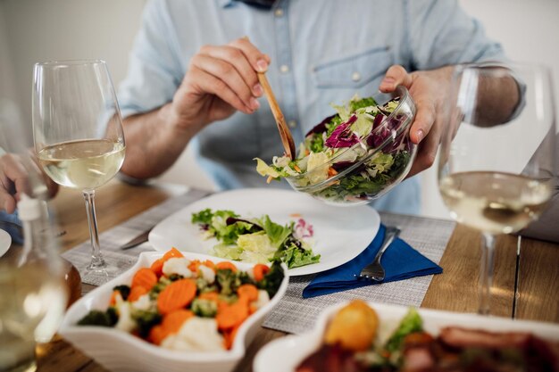 Closeup de homem irreconhecível derramando salada em um prato enquanto almoçava na mesa de jantar