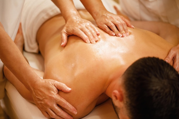 Closeup de homem tendo massagem nas costas por dois terapeutas no spa