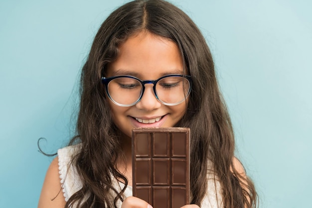 Foto grátis closeup de linda garota tentada enquanto olhava para a barra de chocolate contra o fundo turquesa