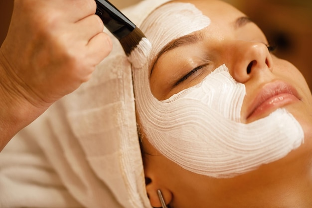 Closeup de linda mulher recebendo máscara facial branca durante o tratamento de spa no salão de beleza