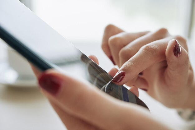 Closeup de mãos femininas com unha vermelha escura manicure usando smartphone