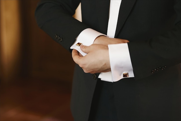 Closeup de mãos masculinas em um smoking consertando a abotoadura do noivo antes da cerimônia de casamento
