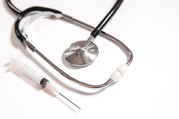 Closeup de medicamentos, seringas e estetoscópio. Imagem de cuidados de saúde limpa e brilhante. Seringa de plástico com agulha isolada no fundo branco