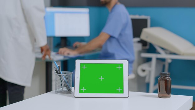 Closeup de mock up computador tablet chave croma de tela verde com display isolado em pé na mesa no escritório do hospital. Equipe médica multiétnica analisando boletim de doença em atendimento à saúde