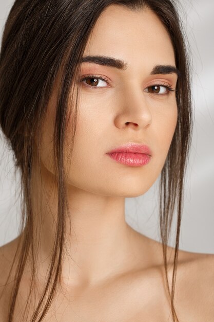 Closeup de mulher atraente com maquiagem natural na parede cinza