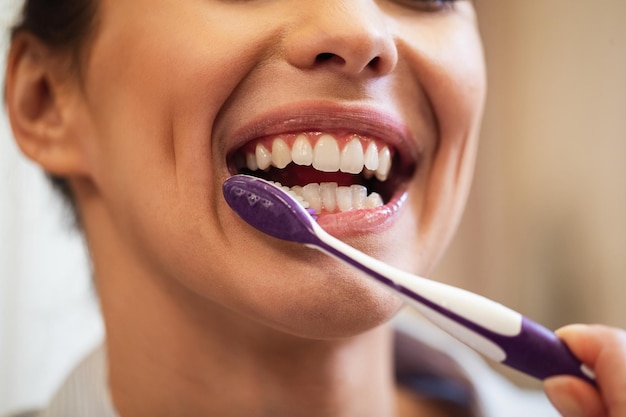 Closeup de mulher usando escova de dentes enquanto escova os dentes no banheiro