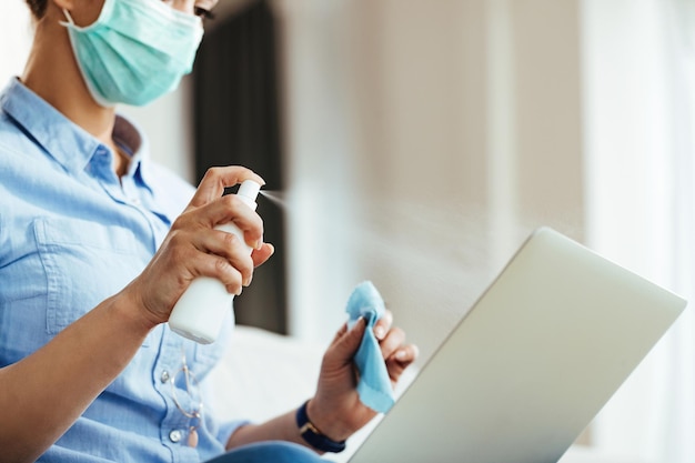 Foto grátis closeup de mulher usando frasco de spray enquanto limpa seu laptop durante epidemia de vírus