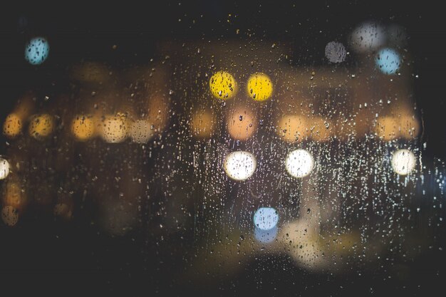 Closeup de pingos de chuva em uma janela de vidro transparente com luzes desfocadas