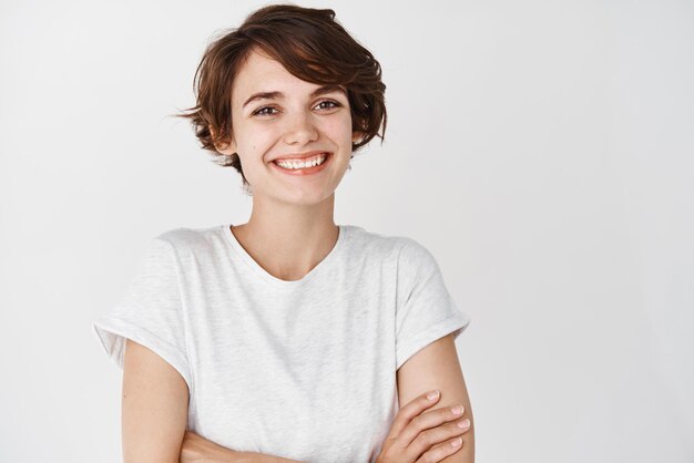 Closeup de uma garota profissional feliz cruzando os braços no peito sorrindo para a câmera fundo branco Copie o espaço