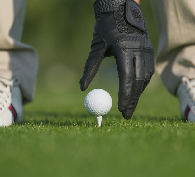 Closeup imagem da mão segurando a bola de golfe com tee no curso mans mão na luva de couro vai tocar a bola isolada no fundo verde