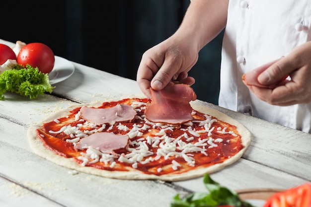 Closeup mão do chef padeiro em uniforme branco, fazendo pizza na cozinha