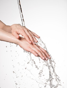 Closeup mãos femininas sob o fluxo de respingos de água - conceito de cuidados com a pele