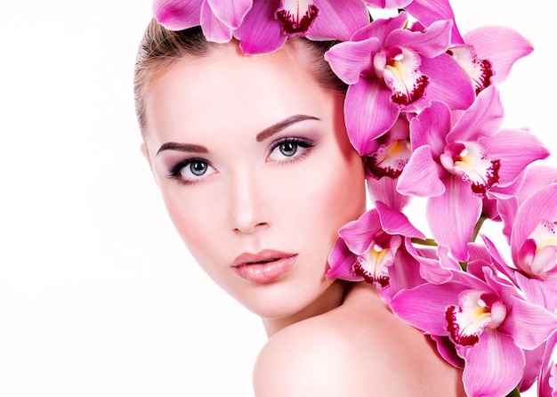 Foto grátis closeup retrato de uma jovem mulher bonita com uma pele limpa e saudável do rosto. menina muito adulta com uma flor perto do rosto. - isolado na parede branca