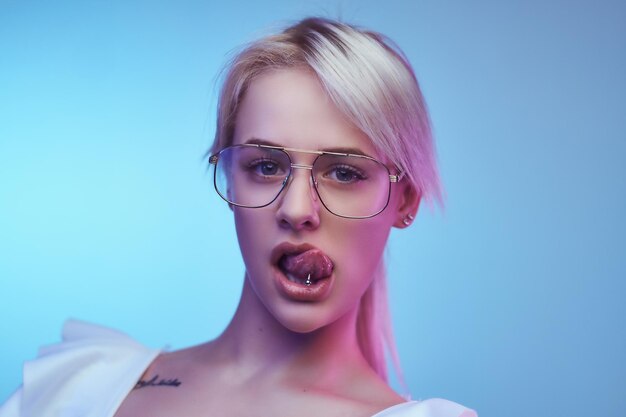 Closeup retrato de uma loira apaixonada usando poses de óculos com a língua saindo olhando para a câmera. Isolado em um fundo azul