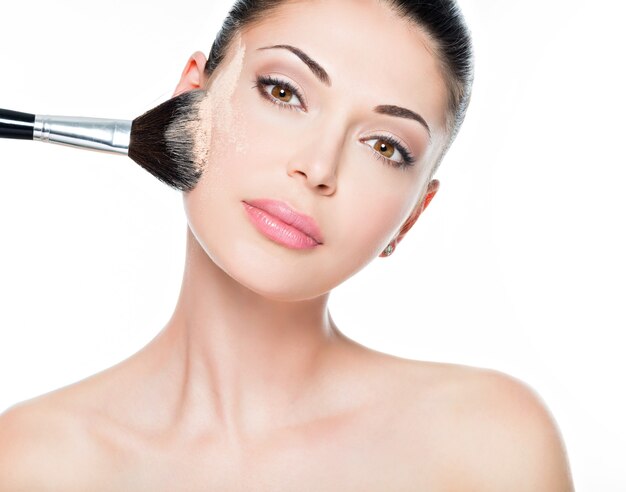 Closeup retrato de uma mulher aplicando base tonal cosmética seca no rosto usando o pincel de maquiagem.