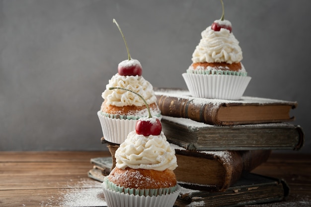 Foto grátis closeup shot de deliciosos cupcakes com creme, açúcar de confeiteiro e uma cereja no topo dos livros