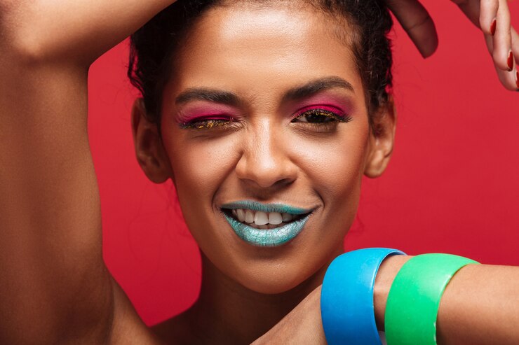 Foto grátis closeup sorrindo mulher afro-americana com maquiagem moda olhando na câmera mostrando as mãos com pulseiras, parede vermelha