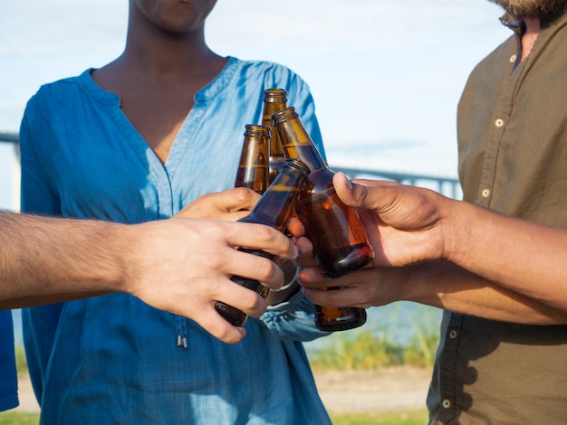 Closeup tiro de amigos tilintar de garrafas de cerveja. grupo de jovens relaxantes depois do trabalho. conceito celebração