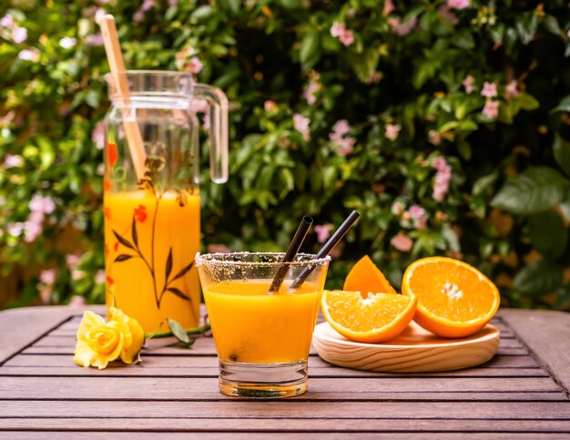 Closeup tiro de suco de laranja fresco com fatias de laranja cortadas em uma mesa de madeira ao ar livre