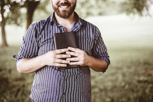 Closeup tiro de um homem sorrindo e segurando a bíblia com um fundo desfocado