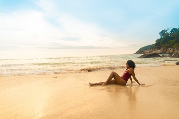 Closeup tiro de um modelo vestindo um maiô vermelho, sentado na praia