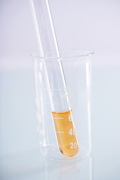 Closeup tiro de um tubo de ensaio com um líquido amarelo dentro de um copo em uma superfície branca
