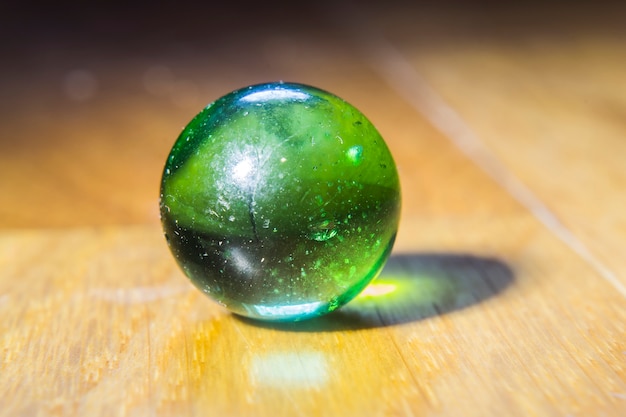 Foto grátis closeup tiro de uma bola de gude verde em cima de uma mesa de madeira