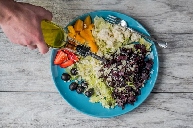 Closeup tiro de uma salada de legumes e frutas com uma pessoa derramando óleo vegetal nele