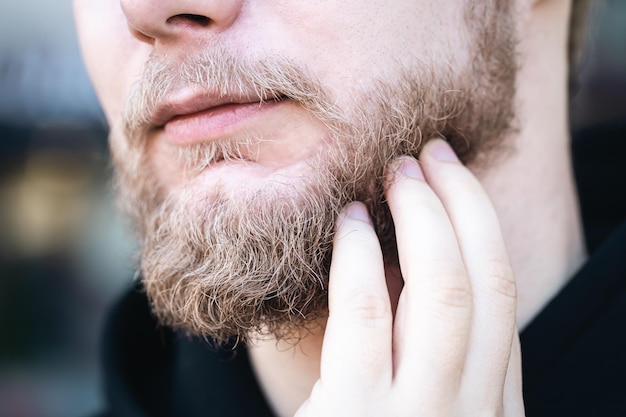 Closeup um jovem toca sua barba com a mão