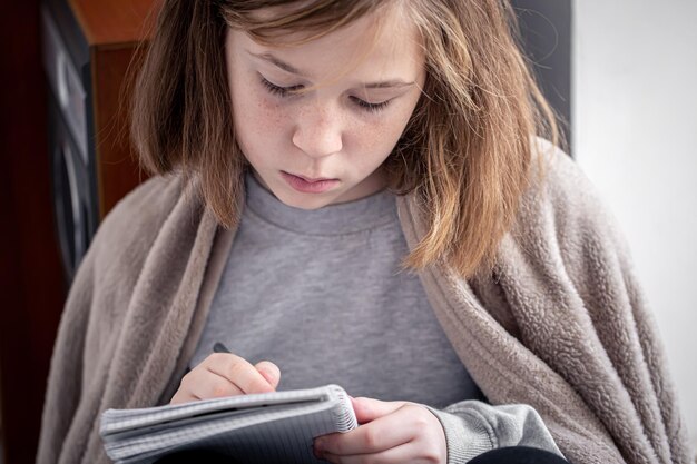 Closeup uma menina desenhando em um caderno embrulhado em uma manta