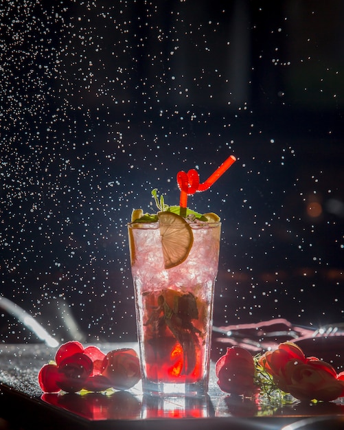 Cocktail de limão berry com tubulação vermelha e cubos de gelo em fundo preto estrelado.