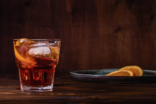 Cocktail Negroni com gelo e uma fatia de laranja em uma mesa de madeira