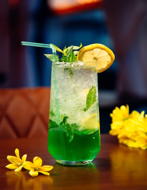 Cocktail verde com hortelã, cubos de gelo e fatia de limão.