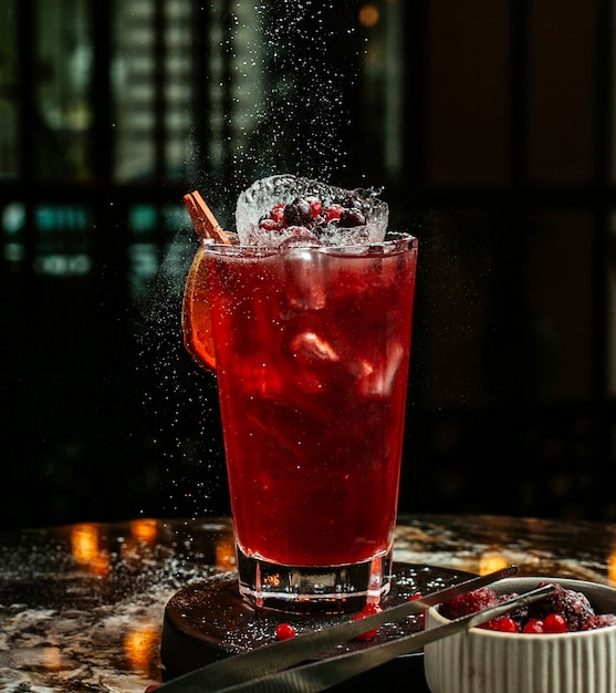 Cocktail vermelho com cubos de gelo e frutas.