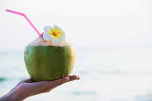 Foto grátis coco fresco na mão com plumeria decorado na praia com a onda do mar - turista com frutas frescas e conceito do mar areia sol férias