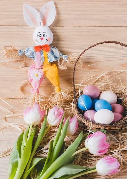 Coelho de brinquedo perto de ovos e tulipas