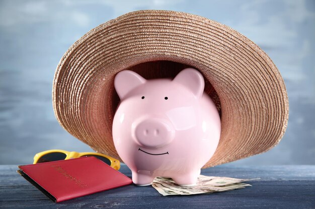 Cofrinho rosa no chapéu de palha com dinheiro, passaporte e óculos de sol sobre fundo azul