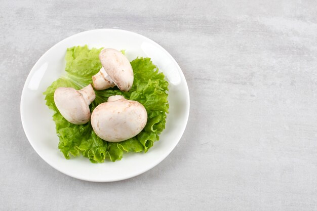 Cogumelos em uma folha de alface em um prato, na mesa de mármore.