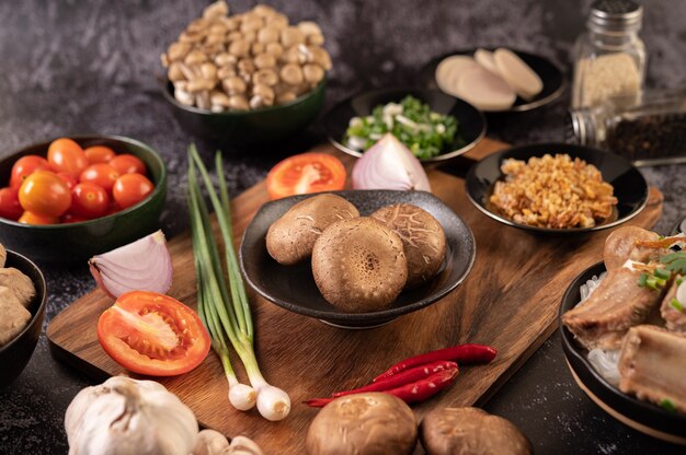 Cogumelos shiitake com alho, tomate, pimentão, cebolinha e cebola roxa em um piso de cimento preto.