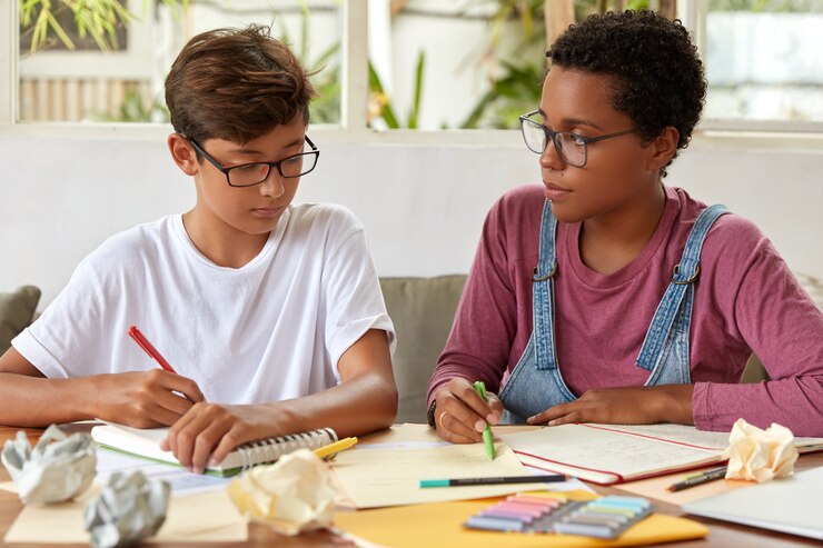 Foto grátis colega de raça mista estudam juntos, escrevem em um caderno, reescrevem informações de papéis, se preparam para o exame da escola, usam roupas casuais, posam na mesa, passam tempo juntos. pessoas, conceito de assistência