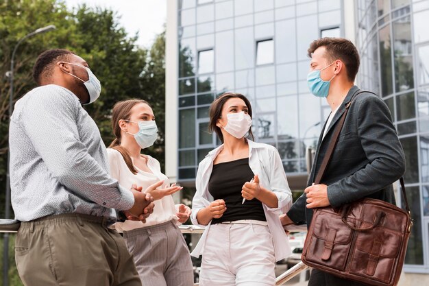 Colegas ao ar livre durante a pandemia conversando com máscaras