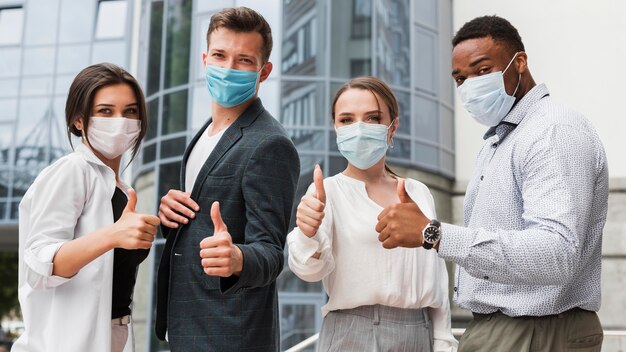 Colegas de trabalho ao ar livre durante a pandemia usando máscaras e dando sinal de positivo