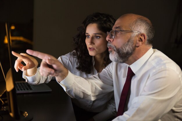 Colegas de trabalho chocados que apontam no monitor do computador