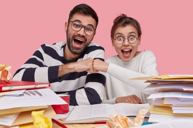 Colegas de trabalho felizes dão um soco no outro, demonstram sua concordância com o projeto, olham positivamente, posam para a mesa com o livro aberto